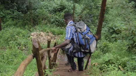 Two-African-men-climb-down-a-dangerous-wooden-ladder-in-a-wet-African-lush-jungle