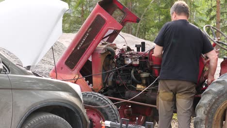 Static-shot-of-a-middle-aged-man-repairing-a-old-tractor-motor,-on-a-sunny,-summer-day,-in-Ostrobothnia,-Finland