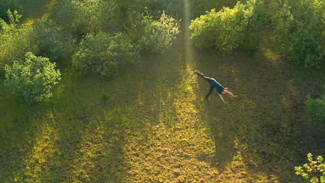 Slow-motion-drone-footage-of-teenage-boy-doing-a-forward-flip,-surrounded-by-green-vegetation