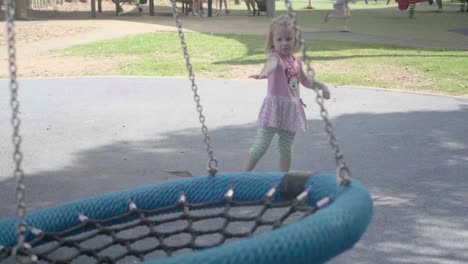 Slow-motion-of-a-young-4-years-old-girl-dressed-in-pink-is-playing-with-a-swinger-in-a-playground-during-a-sunny-day