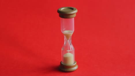 Time-slipping-away-from-a-tiny-sand-timer-on-chroma-red