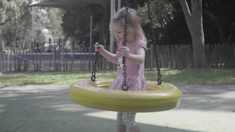 Wide-shot-of-a-4-years-old-girl-playing-with-a-swing-in-a-playground-in-slow-motion