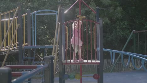 Wide-shot-of-a-4-year-old-girl-in-pink-playing-on-a-structure-in-a-playground