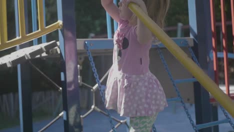 Shot-in-slow-motion-of-a-4-years-old-girl-climbing-a-structure-in-a-playground-during-a-sunny-day