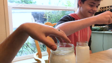 Teenage-boy-smiling-while-painting-mason-jars-at-home-with-his-brother