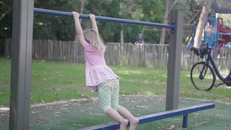 Wide-shot-of-a-4-years-old-girl-in-slow-motion-in-a-playground-who-is-swinging-on-a-bar-and-then-jumping