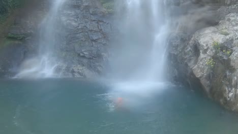 young-man-jumping-in-waterfall-from-cliff-at-morning-from-flat-angle