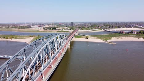 Train-crosses-Bridge-and-Waal-river-in-Nijmegen,-Gelderland,-Netherlands---Aerial
