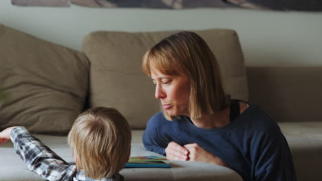 Young-boy-and-mother-reading-a-book-while-sitting-next-to-the-sofa