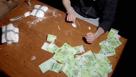 Wealthy-European-Man-Forming-Lines-Of-Cocaine-Powder-On-The-Table-With-Scattered-Dirty-Money