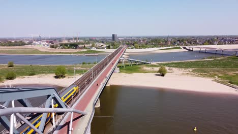 Train-passes-Bridge-and-Waal-river-in-Nijmegen,-Gelderland,-Netherlands---Aerial