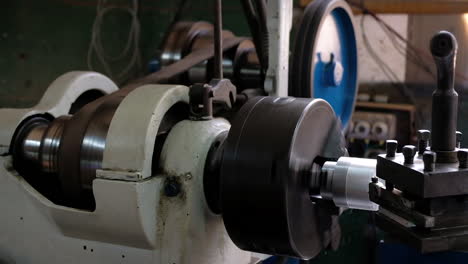 Old-Lathe-with-spinning-pulley-and-machining-an-aluminum-piece-leaving-shaving-long-shot-slow-motion