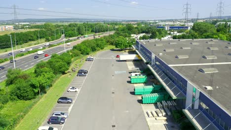 Aerial-moving-shot-of-a-logistics-warehouse-huged-by-a-highway-and-power-lines-close-to-Paris,-France