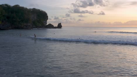 Cinematic-shot-of-people-chilling-in-the-water-and-surfing-at-a-exotic-beach-during-sunset-and-golden-hour