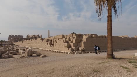 View-of-tourists-walking-and-looking-at-remains-of-the-Karnak-temple-walls,-pieces-of-sandstone-on-the-floor,-archaeological-site