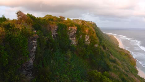 Aerial-pan-of-forested-cliffs-by-ocean-in-evening-sunlight,-Indonesia