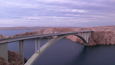 Pag-Bridge-arch-crossing-above-sea-strait,-aerial