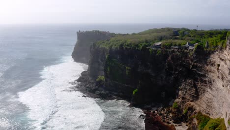 Small-waves-hitting-the-cliff-shore-line-with-lush-greenery-of-Uluwatu-cliffs-in-Bali-on-a-sunny-day