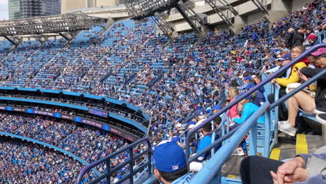 Supporters-Fans-in-Stadium-Stands-Supporting-Blue-Jays-Baseball-Club-Team-of-Toronto,-Crowd-of-Spectators-Watching-Game-During-Sports-Event,-Having-Seats-in-Bleachers,-Stadium-Wave
