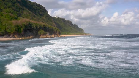 Low-forward-aerial-of-ocean-waves-by-tall-forested-cliffs-in-Indonesia