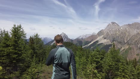 Hiker-walking-trough-pine-trees-on-mountain-range-towards-peak-Rockies-Kananaskis-Alberta-Canada