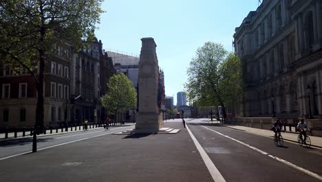 Coronavirus-lockdown---a-few-cyclists-riding-at-lunchtime-pass-the-Cenotaph-on-the-empty-London-street-of-Whitehall---a-normally-busy-tourist-location