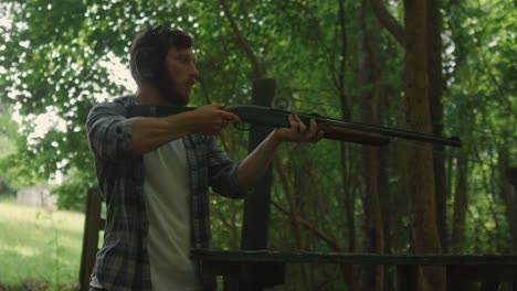 young-American-male-embrace-shotgun-ready-to-shoot-at-the-target-in-the-forest,-focus-training-exercise