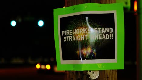 Fireworks-stand-straight-ahead-green-home-made-small-business-sign-posted-stapled-to-telephone-pole-at-night-with-car-lights-bokeh-in-background-as-camera-dolly-pans-left