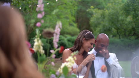 Afroamerikanische-Braut-Und-Bräutigam-Lachen-Während-Ihres-Hochzeitsempfangs-Im-Freien-über-Einen-Insider-Witz-Am-Esstisch