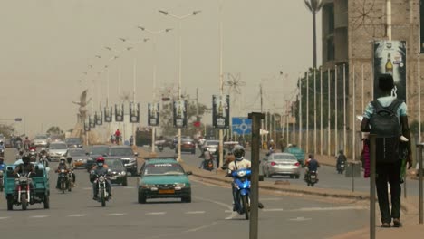 Straßenhändler,-Der-Auf-Dem-Bürgersteig-Mit-Ankommendem-Verkehr-Geht---Togo,-Afrika