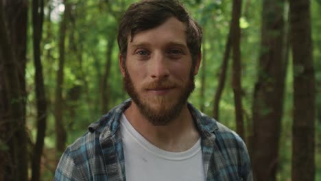 Expressive-bearded-young-man-looking-straight-in-to-the-camera-with-forest-background