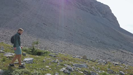 Pan-to-hiker-walking-down-mountain-sun-flare-Rockies-Kananaskis-Alberta-Canada