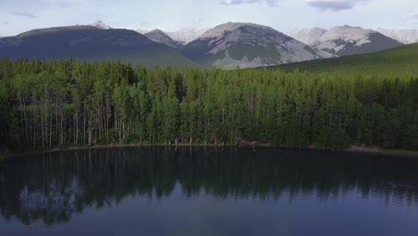 Pond-mountains-and-forest-with-people-in-distance-flyover-Rockies-Kananaskis-Alberta-Canada