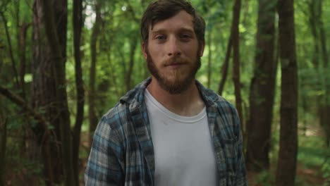 young-caucasian-male-look-up-straight-to-the-camera-standing-in-a-natural-forest-with-tree-on-the-background