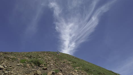 Hiker-ascending-mountain-sky-tilt-clouds,-Rockies,-Kananaskis,-Alberta-Canada