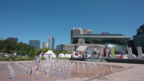 Young-Korean-girl-enjoy-fountain-water-play-in-Seoul-City-Hall-next-to-I-Seoul-U-Symbolic-Sculpture