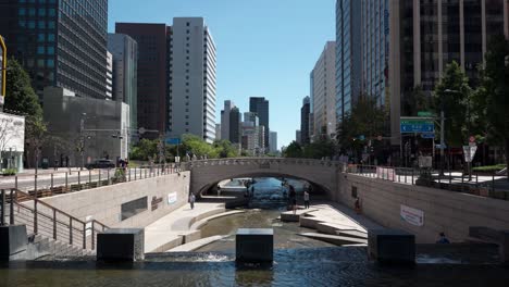 Elevated-View-of-Cheonggyecheon-Waterfall-Water-falling-into-Stream-with-Crowd-of-People-Relaxing-in-Summer