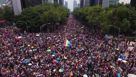 Luftaufnahme-Menschen,-Die-Beim-Gay-Pride-Marsch-In-Der-Sonnigen-Mexiko-Stadt-Eine-Regenbogenfahne-Schwenken---Rückwärts,-Drohnenaufnahme