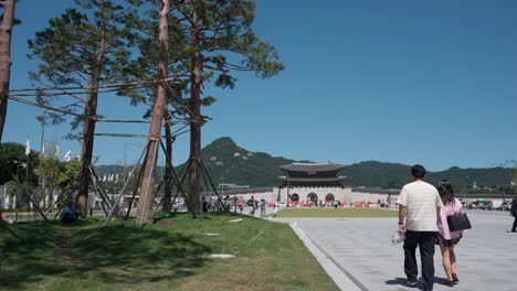 Korean-tourists-stroll-around-at-Gwanghwamun-Plaza,-urban-landscape-of-Gwanghwamun-gate-against-Bugaksan-mountain---copy-space-establishing-shot