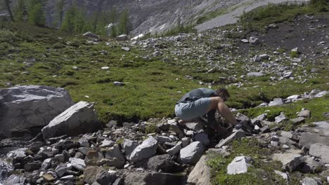 Hiker-drinking-water-from-mountain-stream-pan-tilt,-Rockies-Kananaskis-Alberta-Canada