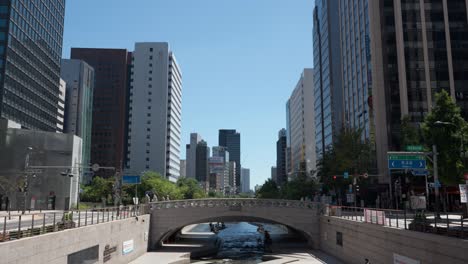 Cheonggyecheon-Stream-Park-with-bridge-and-View-of-High-Glass-Office-Buildings-Exteriors-Against-Blue-Sky---copy-space