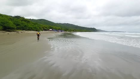 drone-aerial-video-in-nicaragua-beach,-san-juan-del-sur,-palm-,-managua,-rivas,-bicyclist-on-the-beach,-matagalpa,-central-america