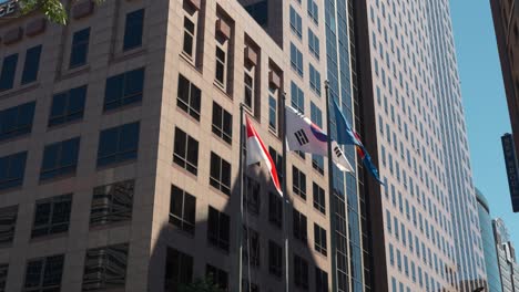 Close-up-of-Flags-of-ASEAN,-Singapore-and-Republic-of-Korea-towering-on-flagpoles-against-SFC---Seoul-Finance-Center-building-facade
