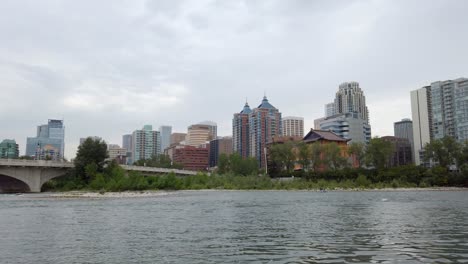 City-river-by-bridge-with-boat-floating-on-cloudy-day-Calgary-Alberta-Canada