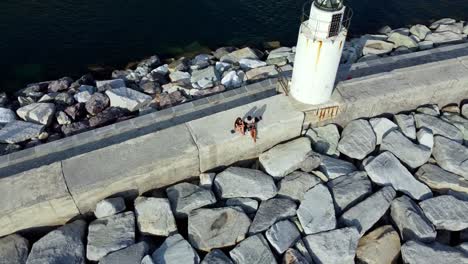 Couple-Sitting-Beside-Old-Lighthouse-in-Camogli-Shore,-Blue-Seascape,-Genova