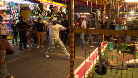 A-crowd-watches-as-a-man-pitches-a-ball-at-a-carnival-game-on-a-summer-evening-at-the-CNE