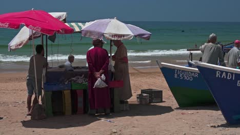 Marokkanische-Fischer-Versammeln-Sich-Um-Einen-Fischerstand-Am-Strand-Von-Taghazout