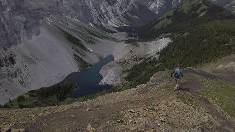 Runner-on-ridge-running-downhill-slipping-by-lake-Rockies-Kananaskis-Alberta-Canada
