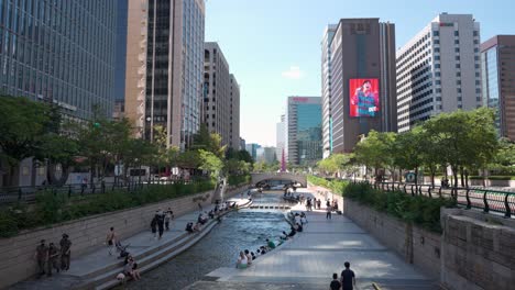 Cheonggyecheon-Stream-Park-Umgeben-Von-Hohen-Bürowolkenkratzern-Mit-Menschen,-Die-Die-Innenstadt-Von-Seoul-Besichtigen-Oder-Sich-Am-Flusswasser-Ausruhen