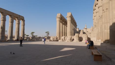 Toma-Panorámica-De-Turistas-Sentados-Y-Explorando-Todo-El-Terreno-Del-Templo-De-Luxor,-Egipto